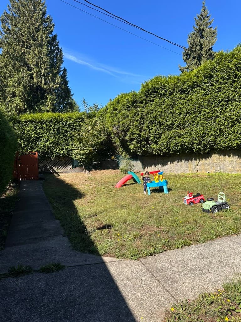 Fenced backyard with a sandbox, ride-on toys, and a grassy play area