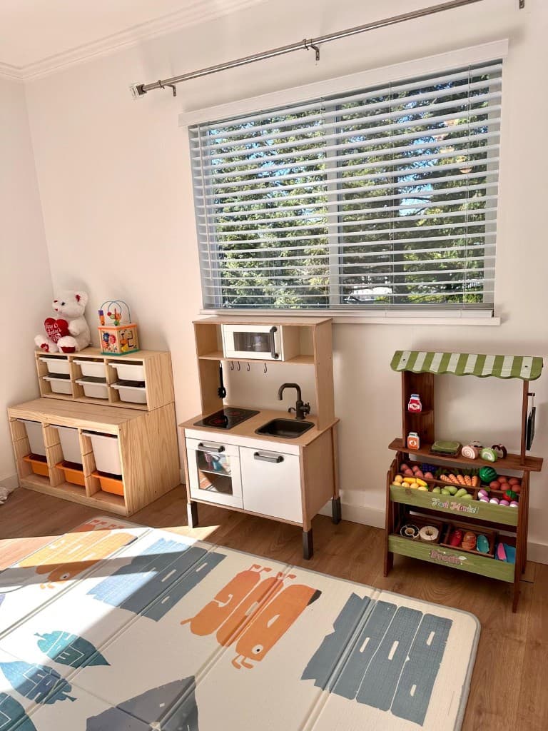 Play kitchen, toy market, and storage bins beside a window